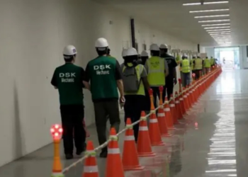 Esta imagem de um vídeo fornecido pelo Serviço de Imigração e Alfândega dos EUA via DVIDS mostra funcionários de uma fábrica esperando para ter as pernas algemadas na fábrica de veículos elétricos do Hyundai Motor Group, quinta-feira, 4 de setembro de 2025, em Ellabell, Geórgia. (Corey Bullard/Serviço de Imigração e Alfândega dos EUA via AP)