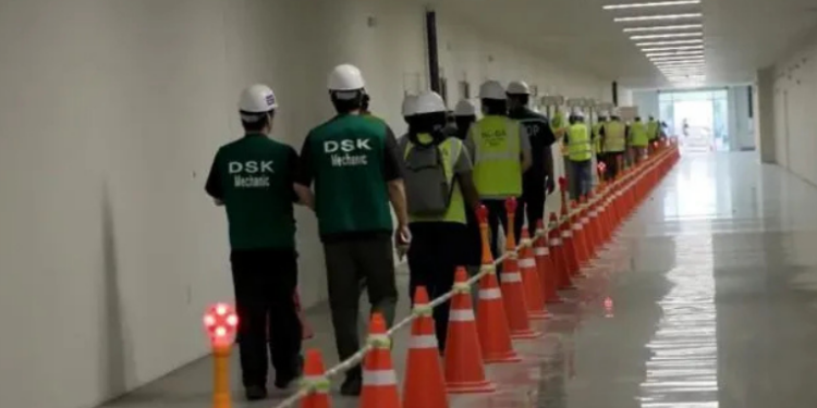 Esta imagem de um vídeo fornecido pelo Serviço de Imigração e Alfândega dos EUA via DVIDS mostra funcionários de uma fábrica esperando para ter as pernas algemadas na fábrica de veículos elétricos do Hyundai Motor Group, quinta-feira, 4 de setembro de 2025, em Ellabell, Geórgia. (Corey Bullard/Serviço de Imigração e Alfândega dos EUA via AP)